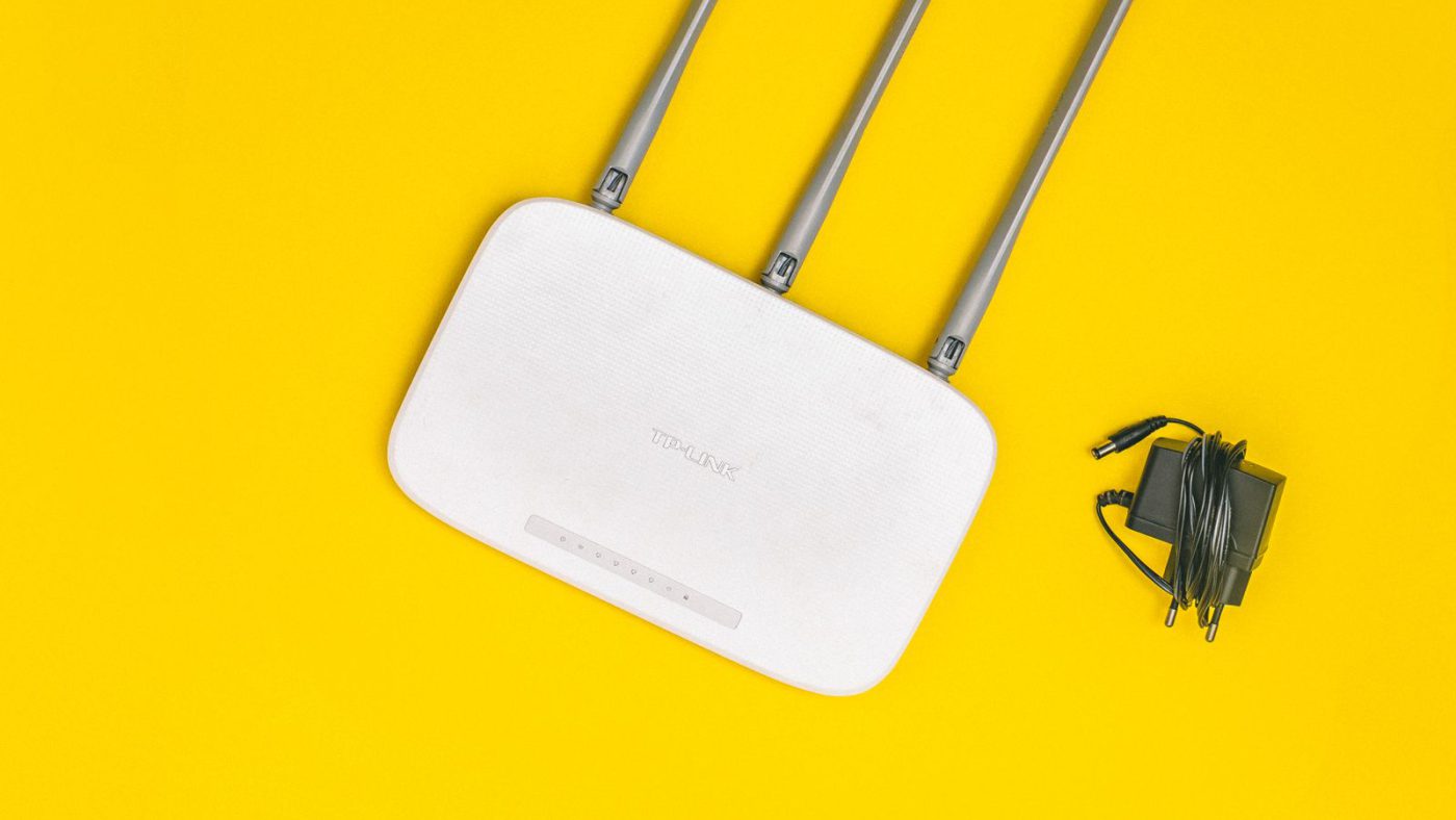 A white Wi-Fi router with external antennas on a yellow background